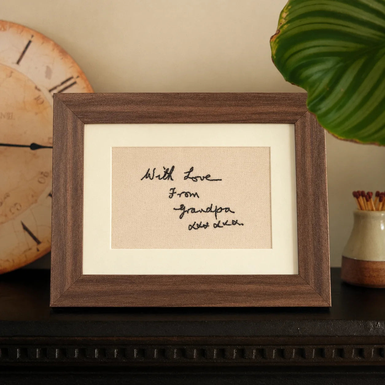 A handwritten family note recreated in black embroidery and displayed in a walnut frame